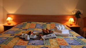 A hotel room with a bed, two bedside lamps, a tray with breakfast items, a newspaper, and a vase with flowers. - Hôtel Restaurant La Diligence (Le Brignon)