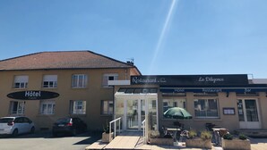 A hotel with a restaurant and bar, featuring a tiled roof, a glass entrance, and outdoor seating with a green umbrella. - Hôtel Restaurant La Diligence (Le Brignon)