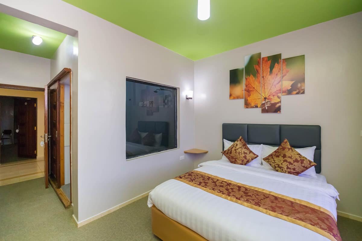 Une chambre d’hôtel avec un lit, une fenêtre, une porte et un mur orné de trois tableaux représentant des feuilles.