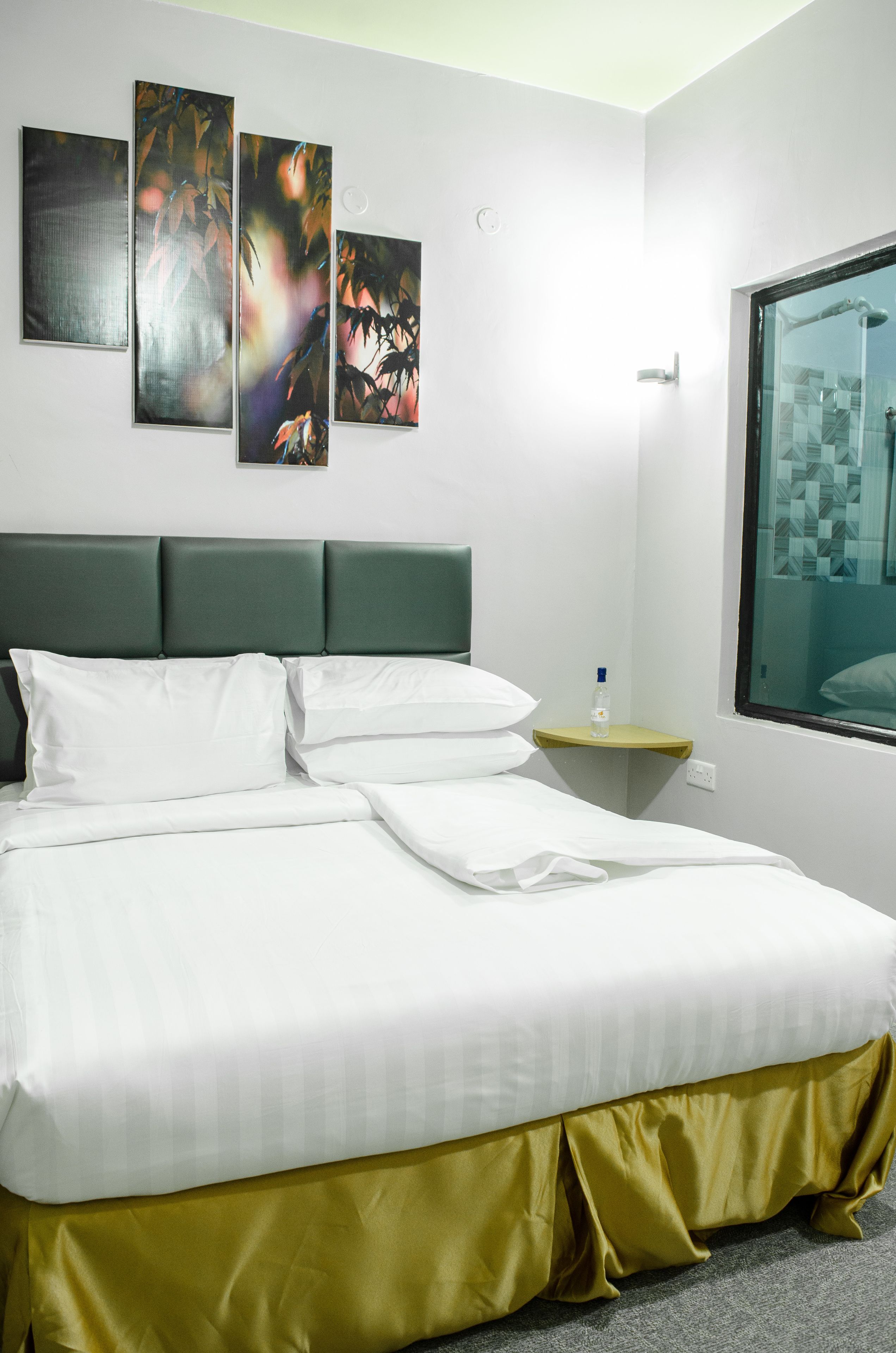 Una habitación de hotel con una cama, una mesita, una botella y obras de arte en la pared.