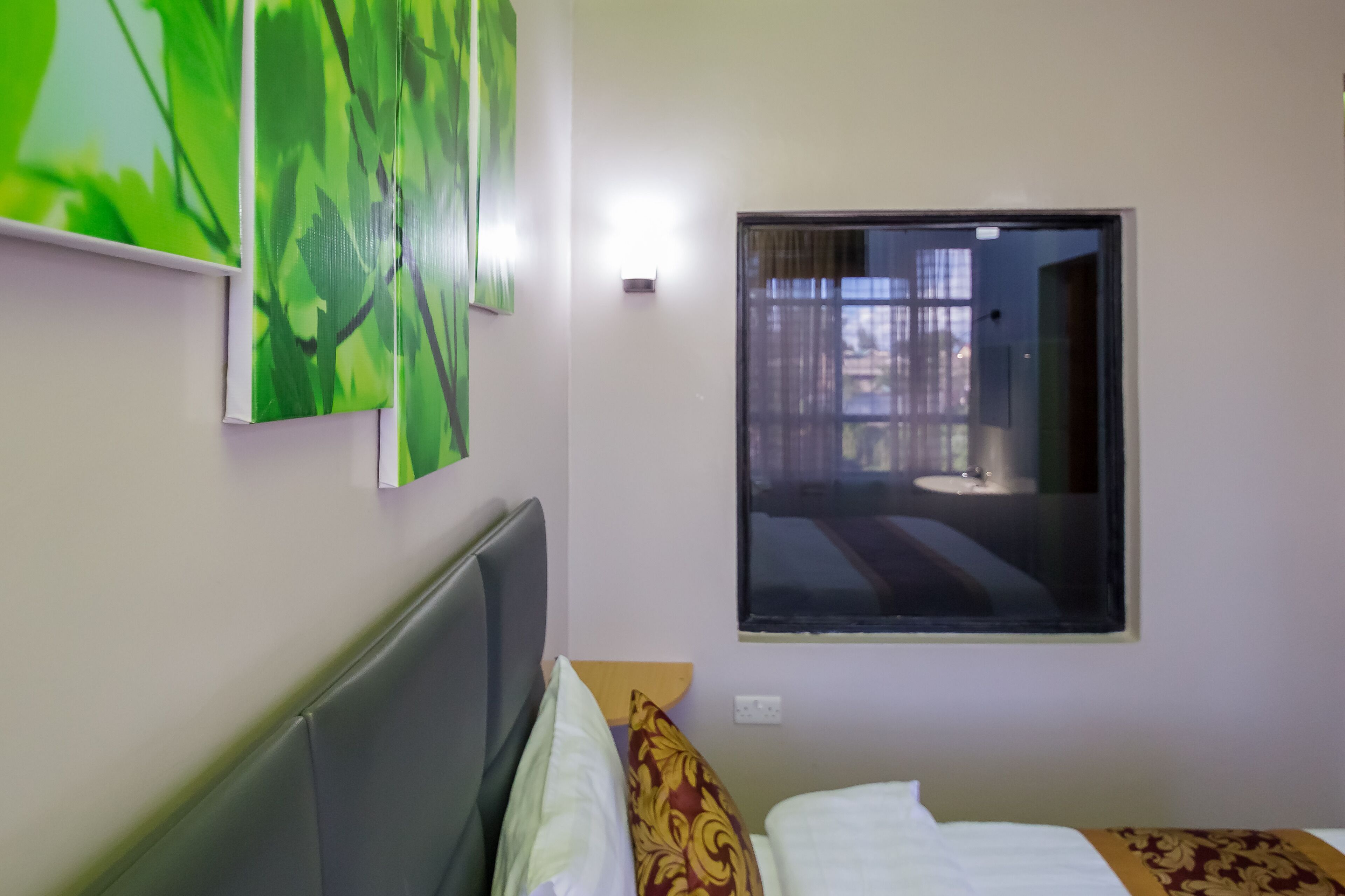 A hotel room with a bed, a headboard, a window, and a wall-mounted light.