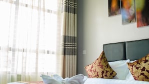 A hotel room with a bed, curtains, and wall art. - Maple Inn Hotel (Ruiru)