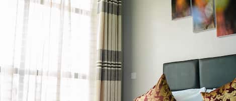 A hotel room with a bed, curtains, and wall art.