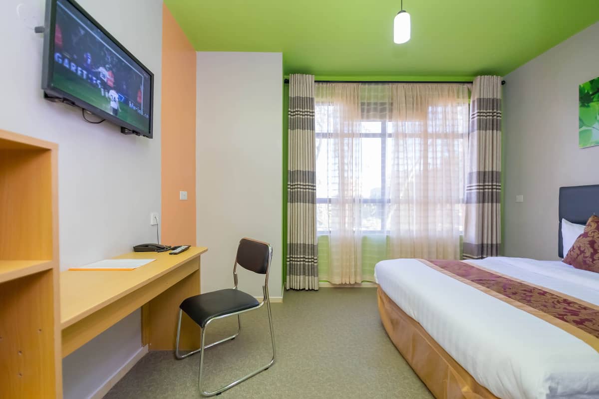 Une chambre d’hôtel avec un lit, un bureau et une chaise, un téléviseur fixé au mur et une fenêtre avec des rideaux.