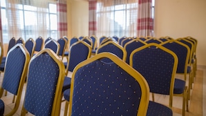 Rows of blue chairs with gold frames in a room with large windows and a chandelier. - Maple Inn Hotel (Ruiru)