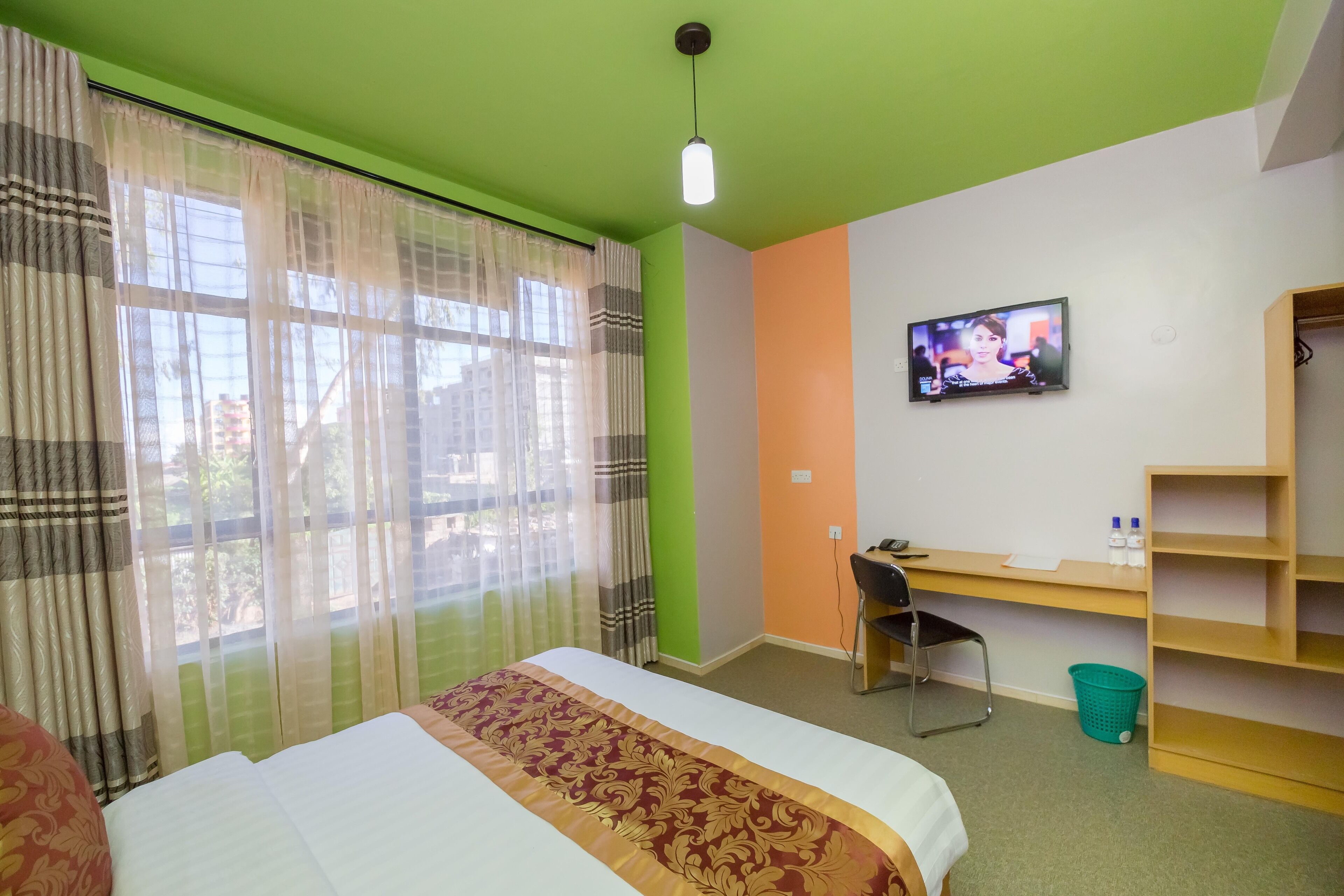 A hotel room with a bed, a desk, a chair, a television, and a window with curtains.