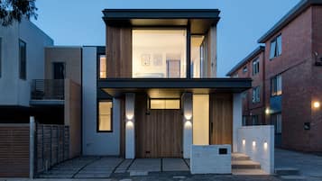 A modern two-story house with a flat roof, large windows, and a wooden front door.