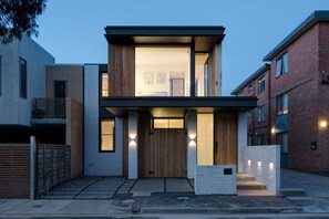 A modern two-story house with a flat roof, large windows, and a wooden front door.