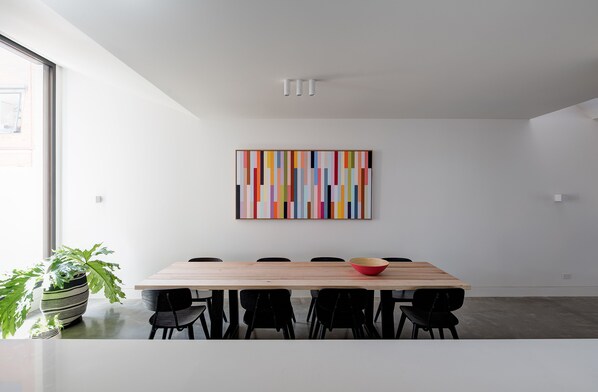 A modern dining area with a wooden table, black chairs, and a colorful abstract painting on the wall.