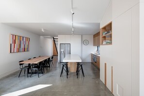 A modern kitchen with a central island, a dining area with a long table and chairs, and a staircase leading to an upper level.