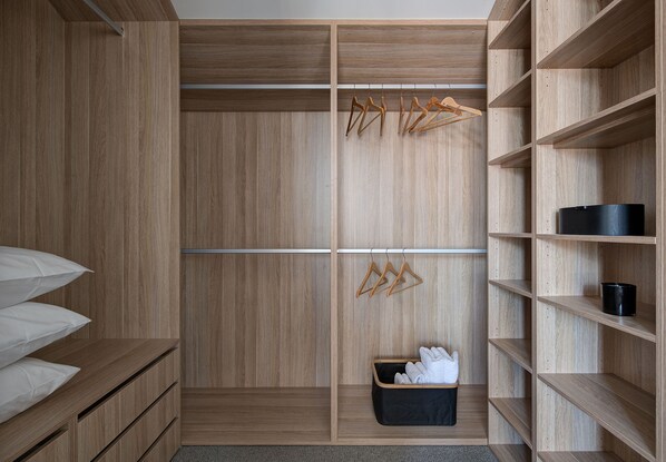 A walk-in closet with wooden shelving, a hanging rack, and a storage bin.