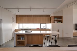 A modern kitchen with a central island, wooden cabinetry, a built-in bookshelf, and a large window providing natural light. - Woodfin House Pet Friendly Home in Abbotsford (Abbotsford)