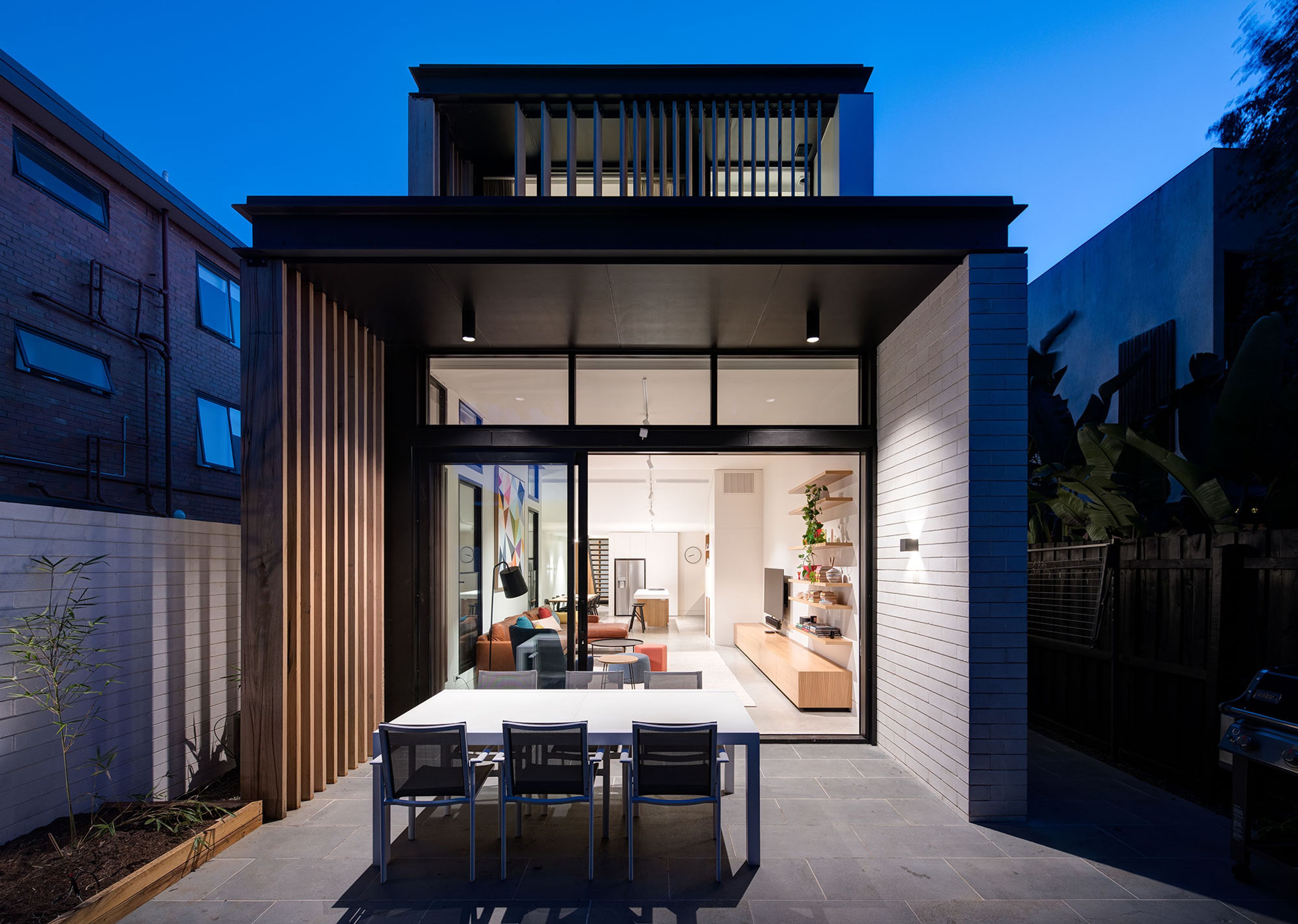 A modern house with a patio, a dining area, and a kitchen visible through the glass doors.