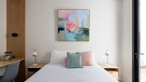 A modern bedroom with a bed, two bedside tables, a desk, a chair, and a large abstract painting on the wall. - Woodfin House Pet Friendly Home in Abbotsford (Abbotsford)