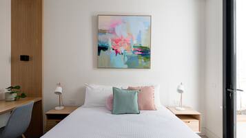 A modern bedroom with a bed, two bedside tables, a desk, a chair, and a large abstract painting on the wall.