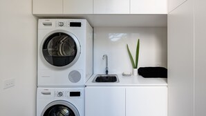A compact laundry area with two Bosch washing machines, a sink, and a small plant. - Woodfin House Pet Friendly Home in Abbotsford (Abbotsford)