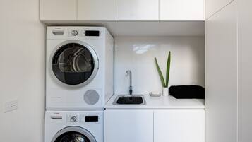 A compact laundry area with two Bosch washing machines, a sink, and a small plant.