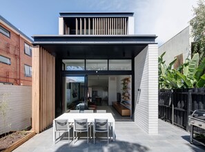 Ein modernes Haus mit Terrasse, Essbereich mit Stühlen und Grill.
