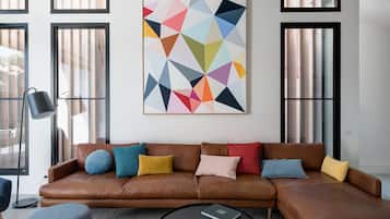 A modern living room with a brown leather sofa, colorful cushions, a black coffee table, and a geometric abstract painting on the wall.