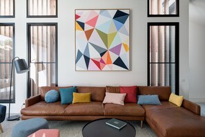 A modern living room with a brown leather sofa, colorful cushions, a black coffee table, and a geometric abstract painting on the wall.