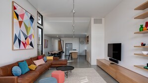 A modern living room with a brown leather sofa, colorful cushions, a coffee table, and a TV on a wooden stand. - Woodfin House Pet Friendly Home in Abbotsford (Abbotsford)