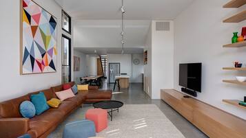 A modern living room with a brown leather sofa, colorful cushions, a coffee table, and a TV on a wooden stand.