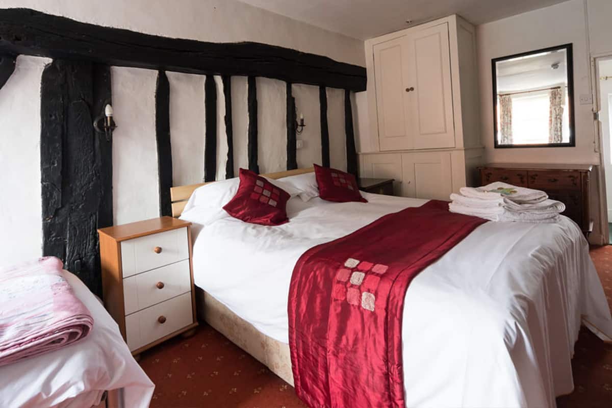 A bedroom with a large bed, a wardrobe, a mirror, and a window with curtains.