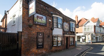 A traditional brick building with multiple signs advertising local food, cask ales, and en-suite rooms.