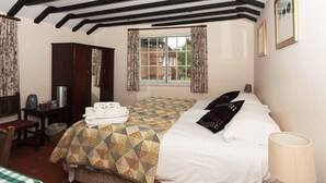 A bedroom with a bed, a desk, a chair, a lamp, and a window with curtains. - The Bull at Wargrave (Reading)