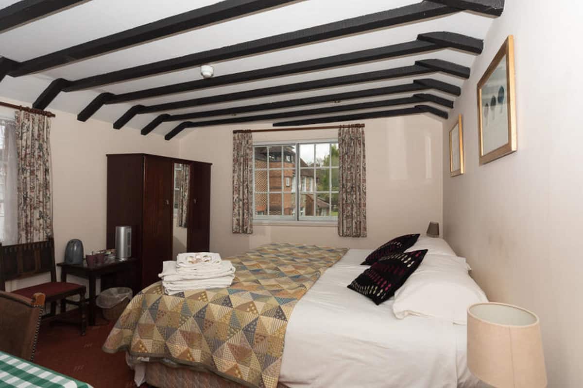 A bedroom with a bed, a desk, a chair, and a window with curtains.