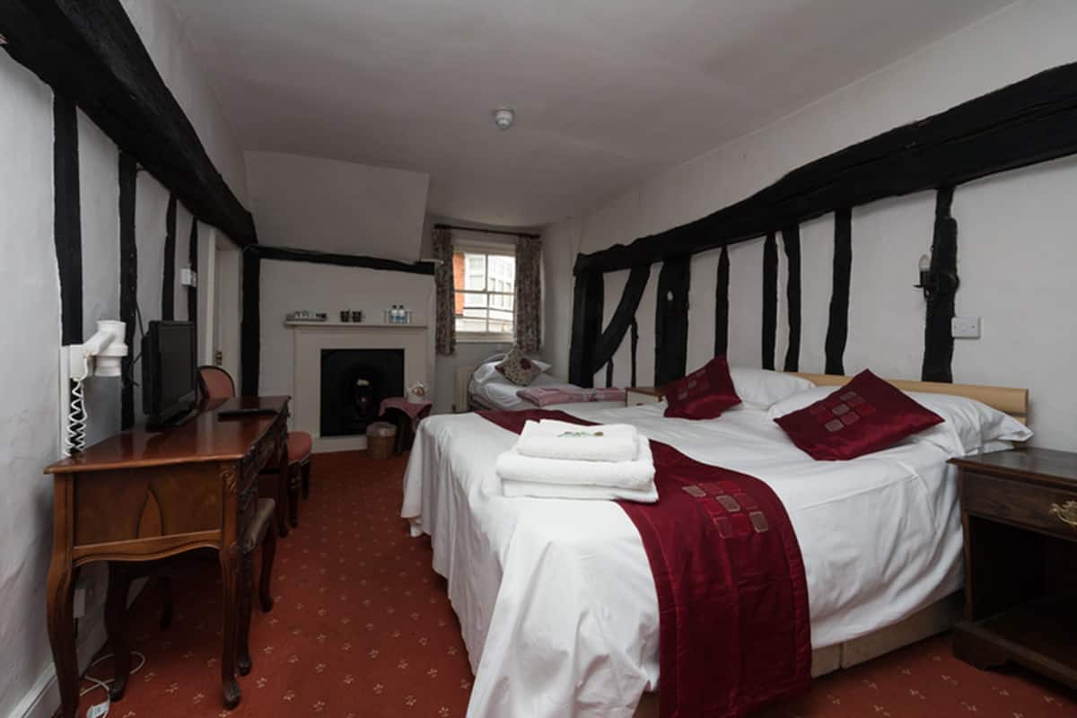 A bedroom with a bed, a desk, a chair, a television, and a fireplace.