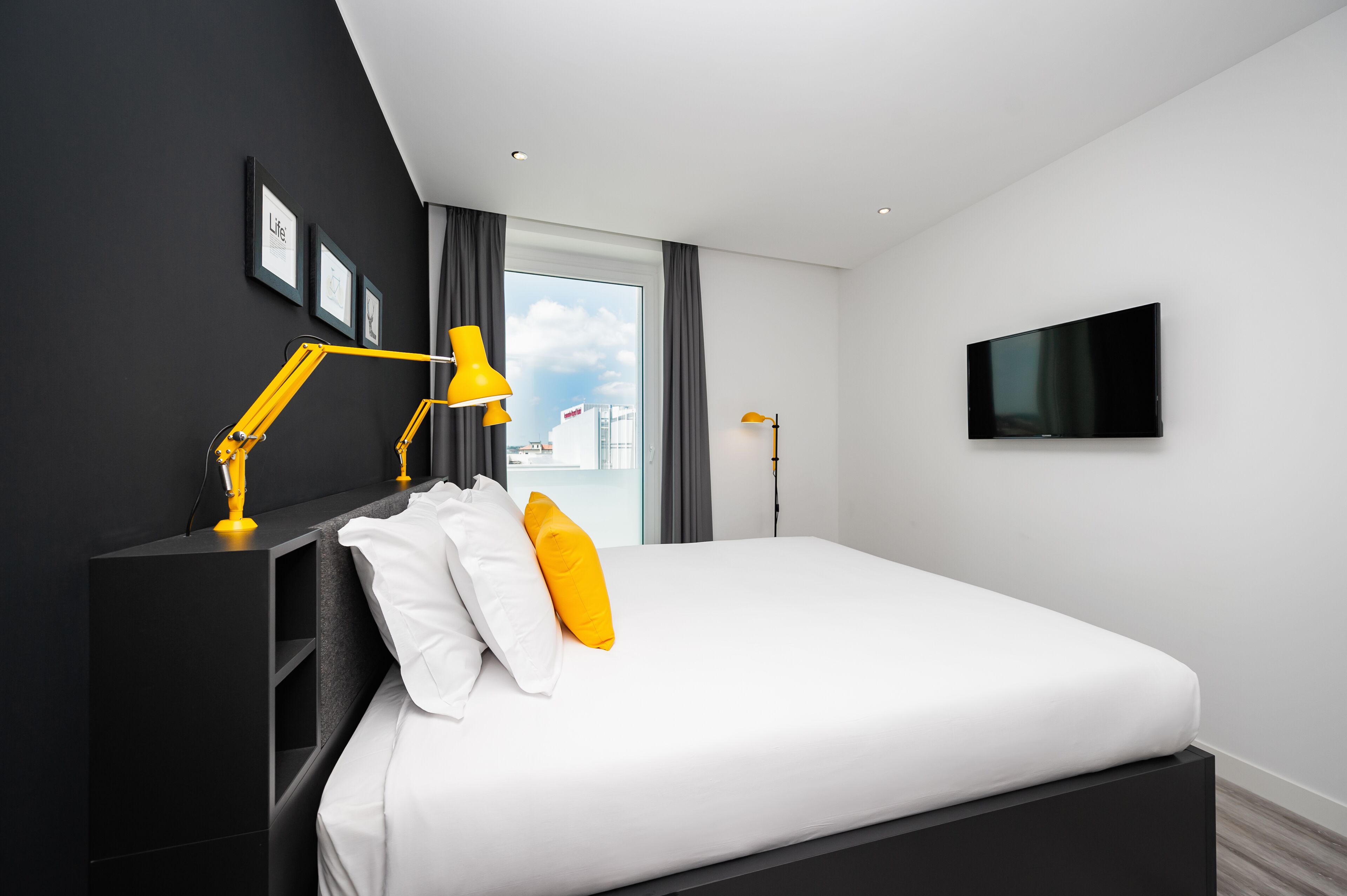 A modern bedroom with a large bed, a flat-screen TV, and a window with curtains.