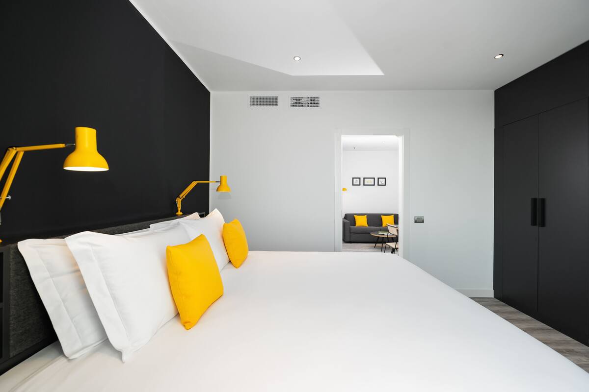 A modern bedroom with a large bed, a black wardrobe, and a bright yellow lamp.
