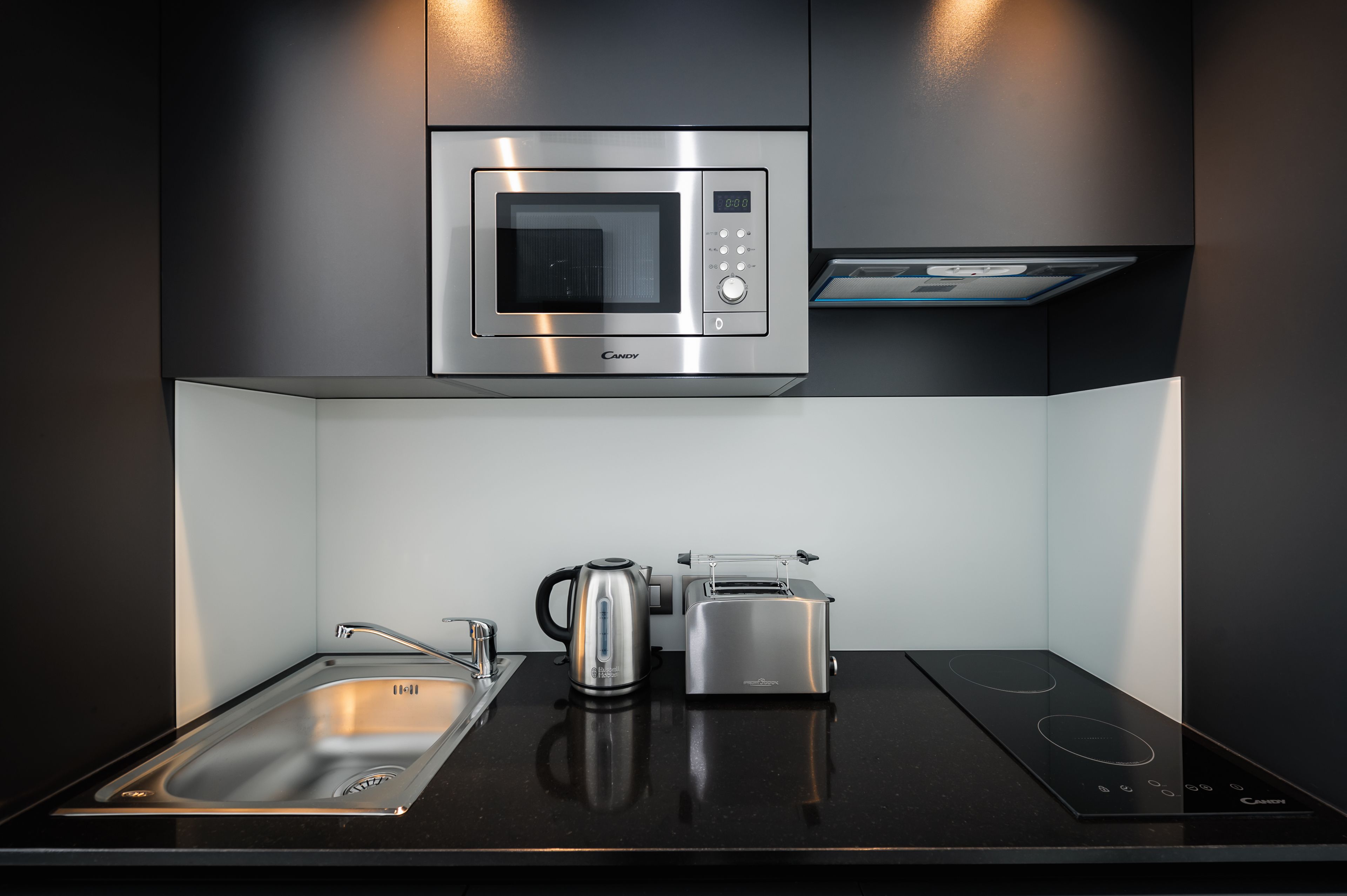 Una cocina moderna con microondas integrado, tostadora, hervidor y placa de inducción.