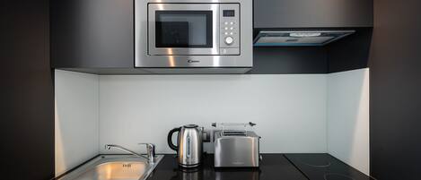 A modern kitchen with a built-in microwave, toaster, kettle, and induction cooktop.