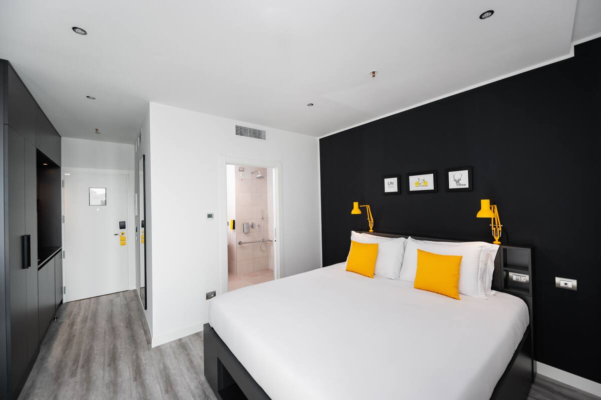 A modern hotel room with a large bed, a black accent wall, and a bright yellow lamp.