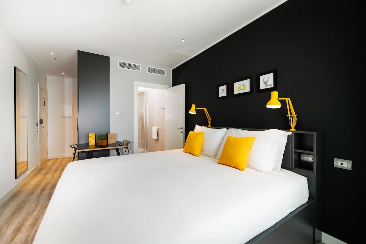 A modern hotel room with a large bed, a desk, and a black accent wall with framed pictures.