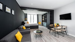 A modern hotel room with a grey sofa, a bed, a dining table with chairs, and a TV mounted on the wall. - Staycity Aparthotels, Venice, Mestre (Mestre)