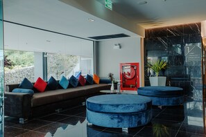 A modern lobby with a sofa, blue ottomans, and a red sign. - Rak Elegant Hotel Patong (Patong)