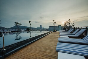 A wooden deck with lounge chairs and a pool, overlooking a cityscape and mountains. - Rak Elegant Hotel Patong (Patong)