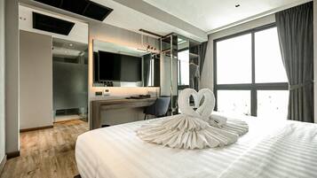 Quarto de hotel com uma cama grande, uma escrivaninha, uma cadeira, uma televisão e uma janela ampla.