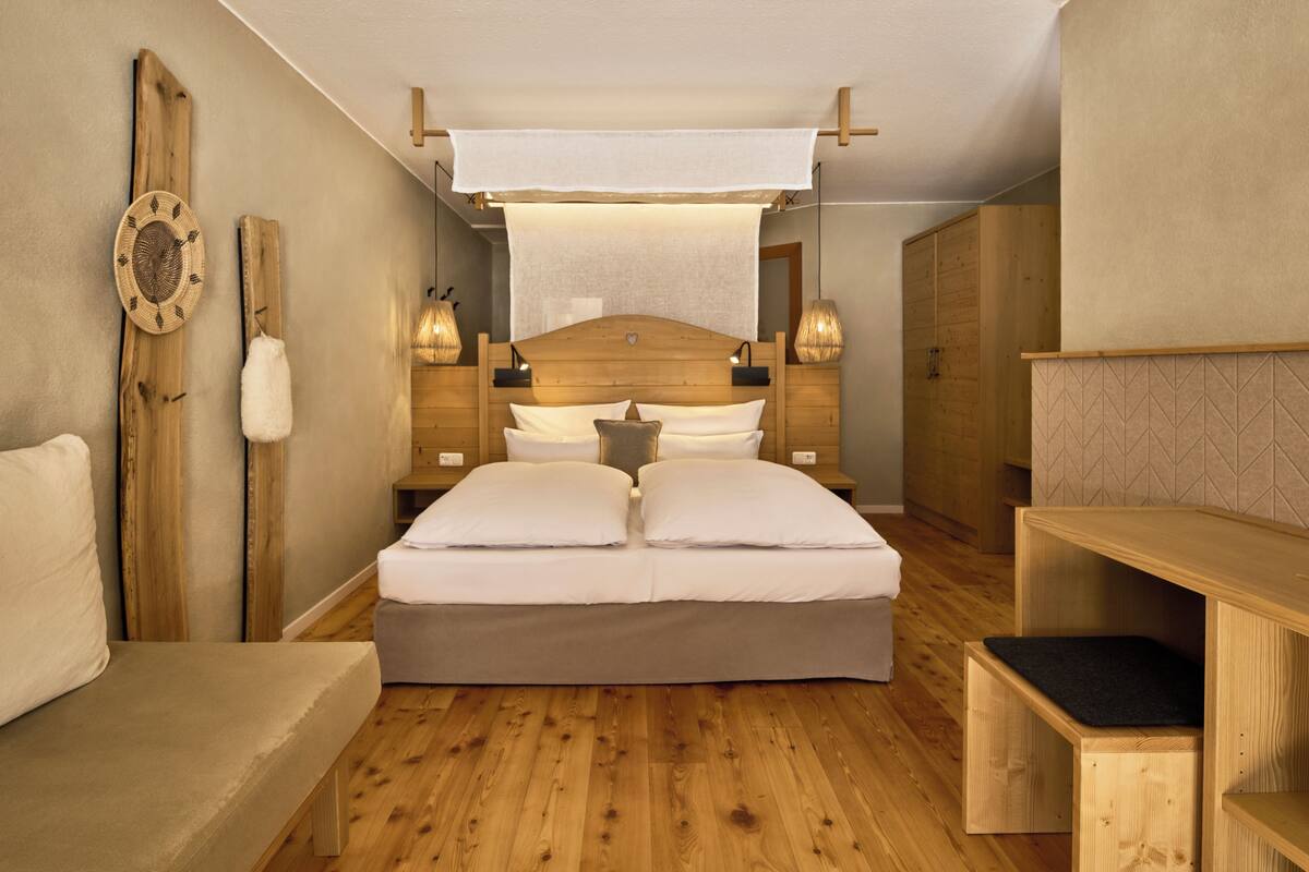 A bedroom with a wooden headboard, a large bed with white bedding, two bedside tables with lamps, and a wooden bench.