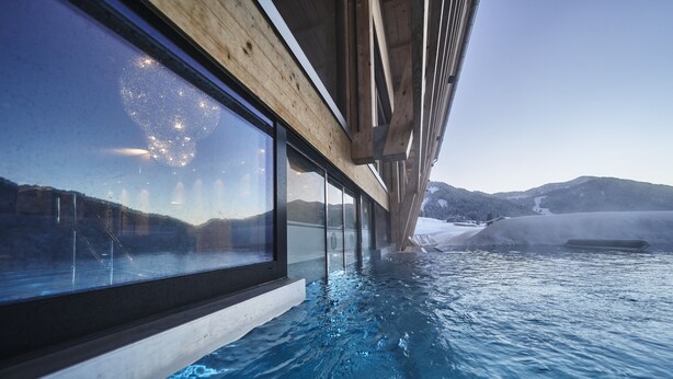 A transparent glass wall of a hot spring bath with a view of a snowy landscape and mountains. - Hubertus Mountain Refugio Allgäu (Balderschwang)