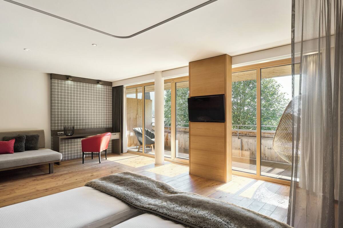 A modern living room with a sofa, a red chair, a flat-screen TV, and a large window offering a view of the outdoors.