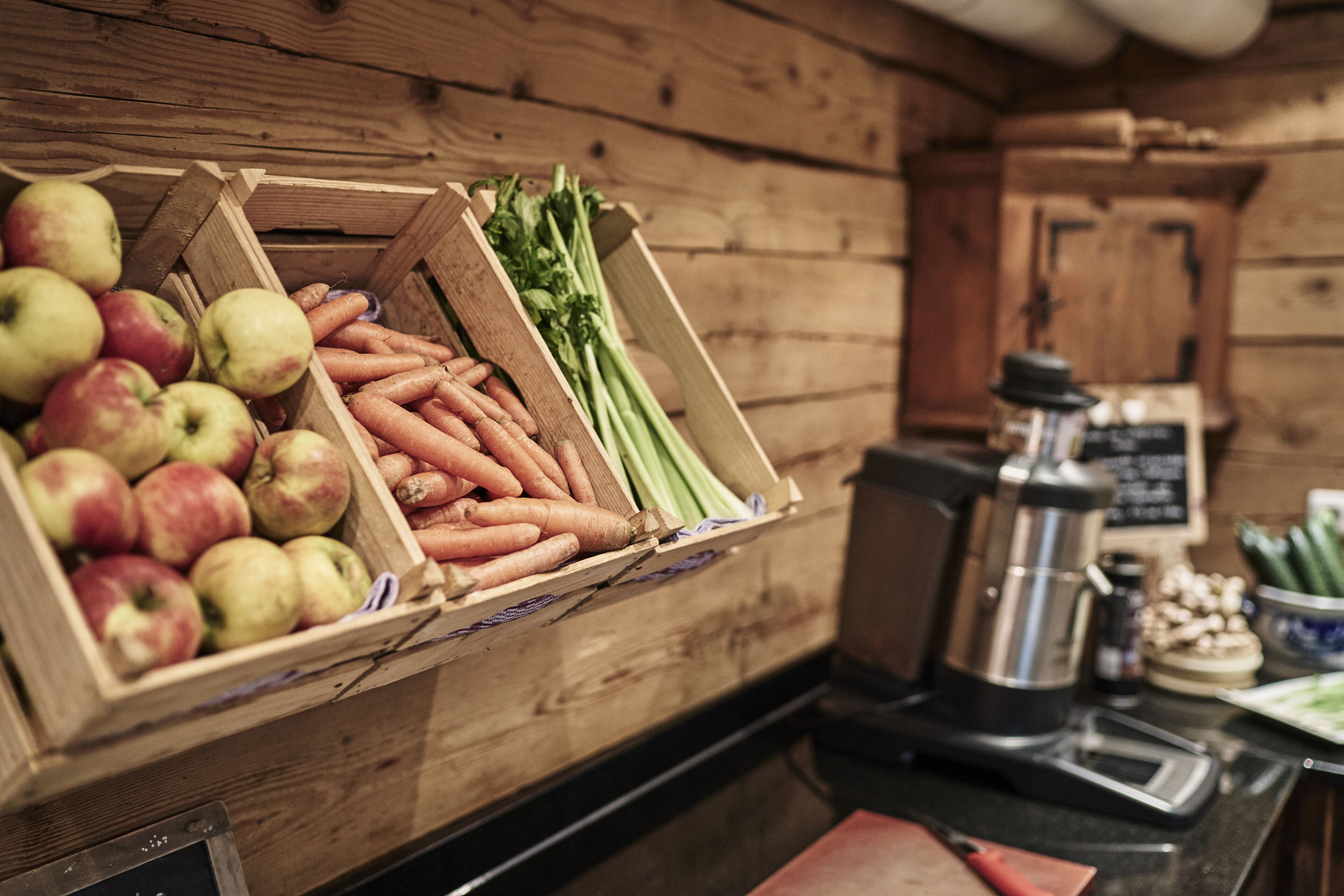 A wooden-framed display of apples, carrots, and celery in a rustic kitchen setting.