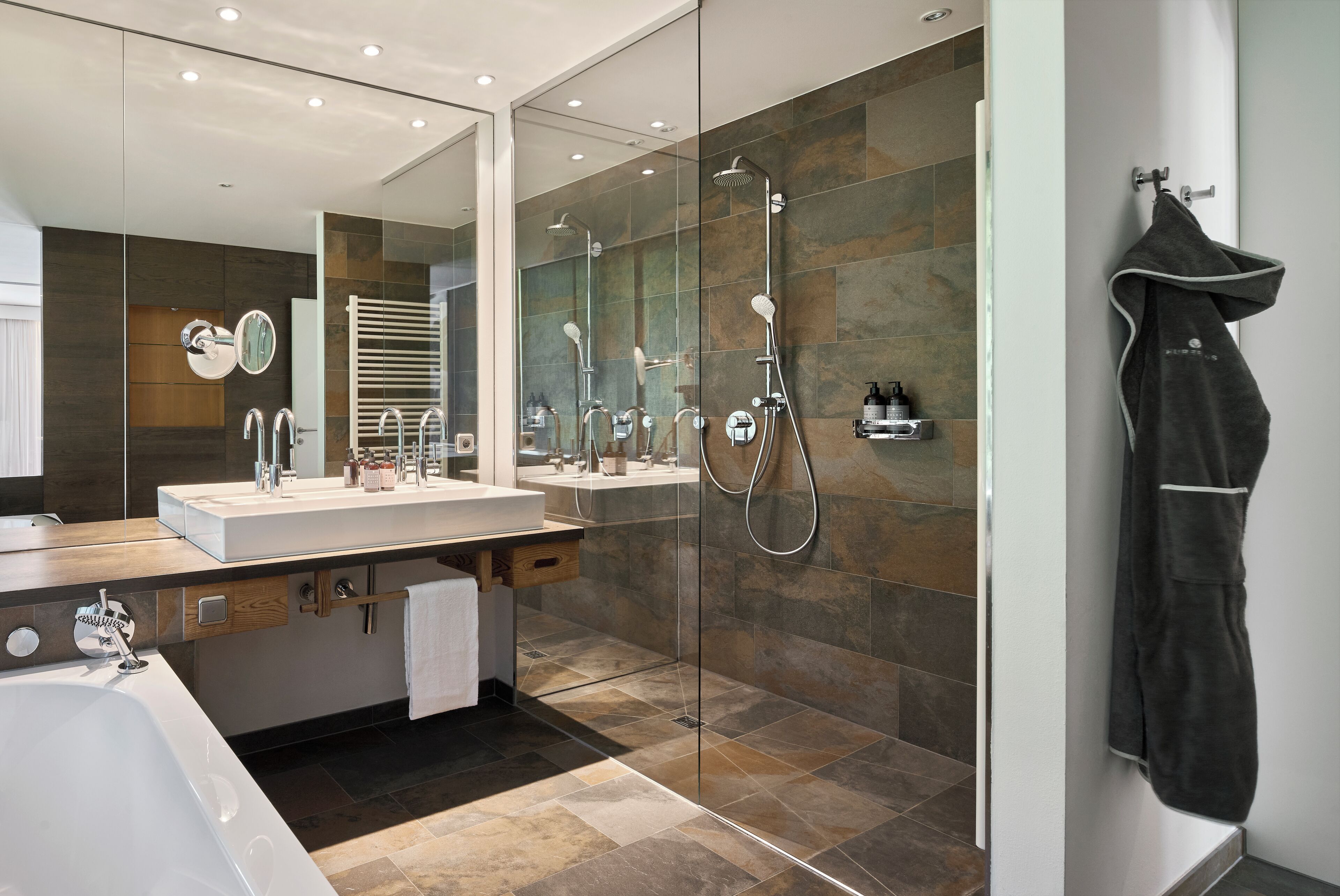 A modern bathroom with a glass-enclosed shower, a large mirror, and a vanity with a sink and towel rack.
