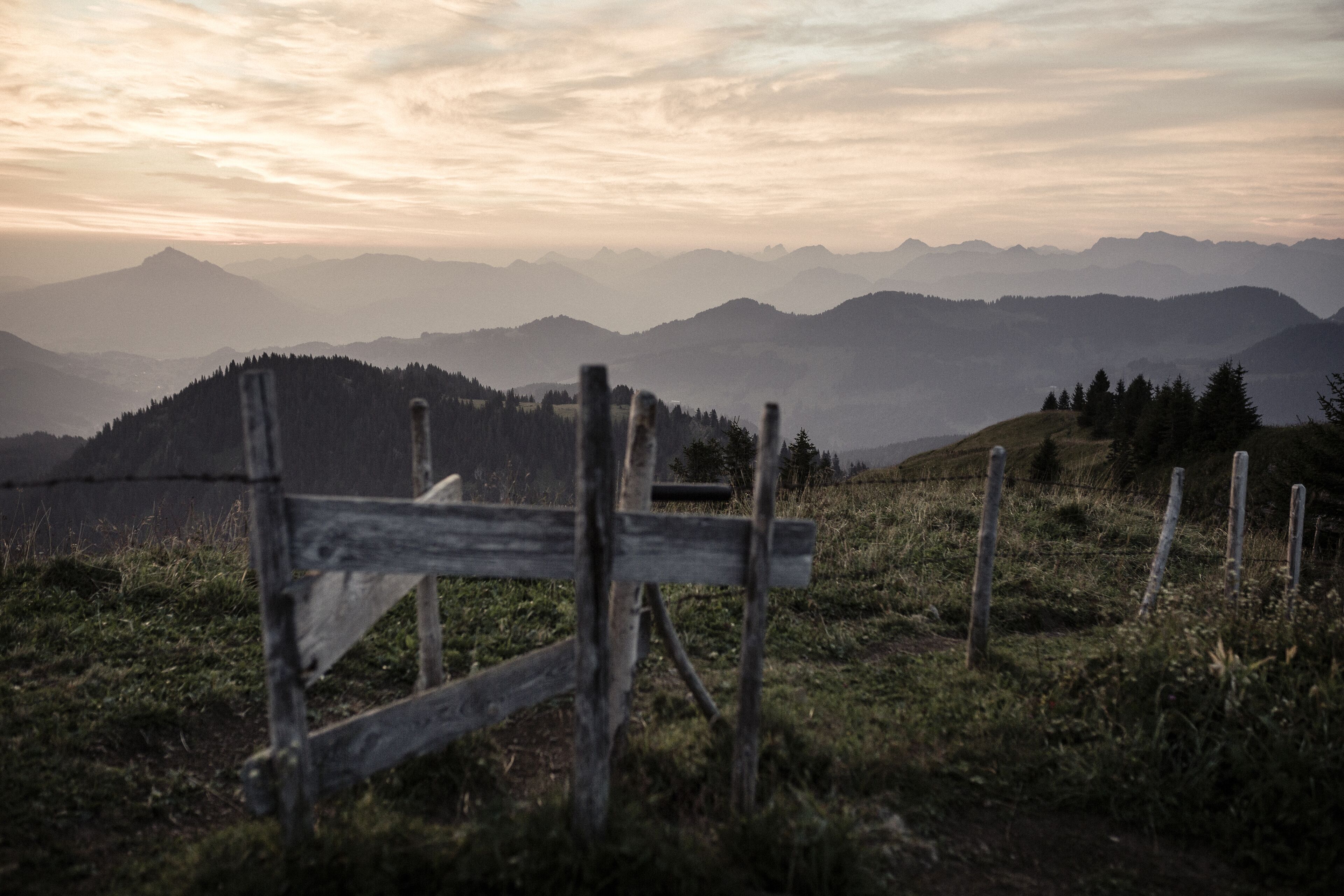 Une clôture en bois dans un champ verdoyant, avec une chaîne de montagnes en arrière-plan.