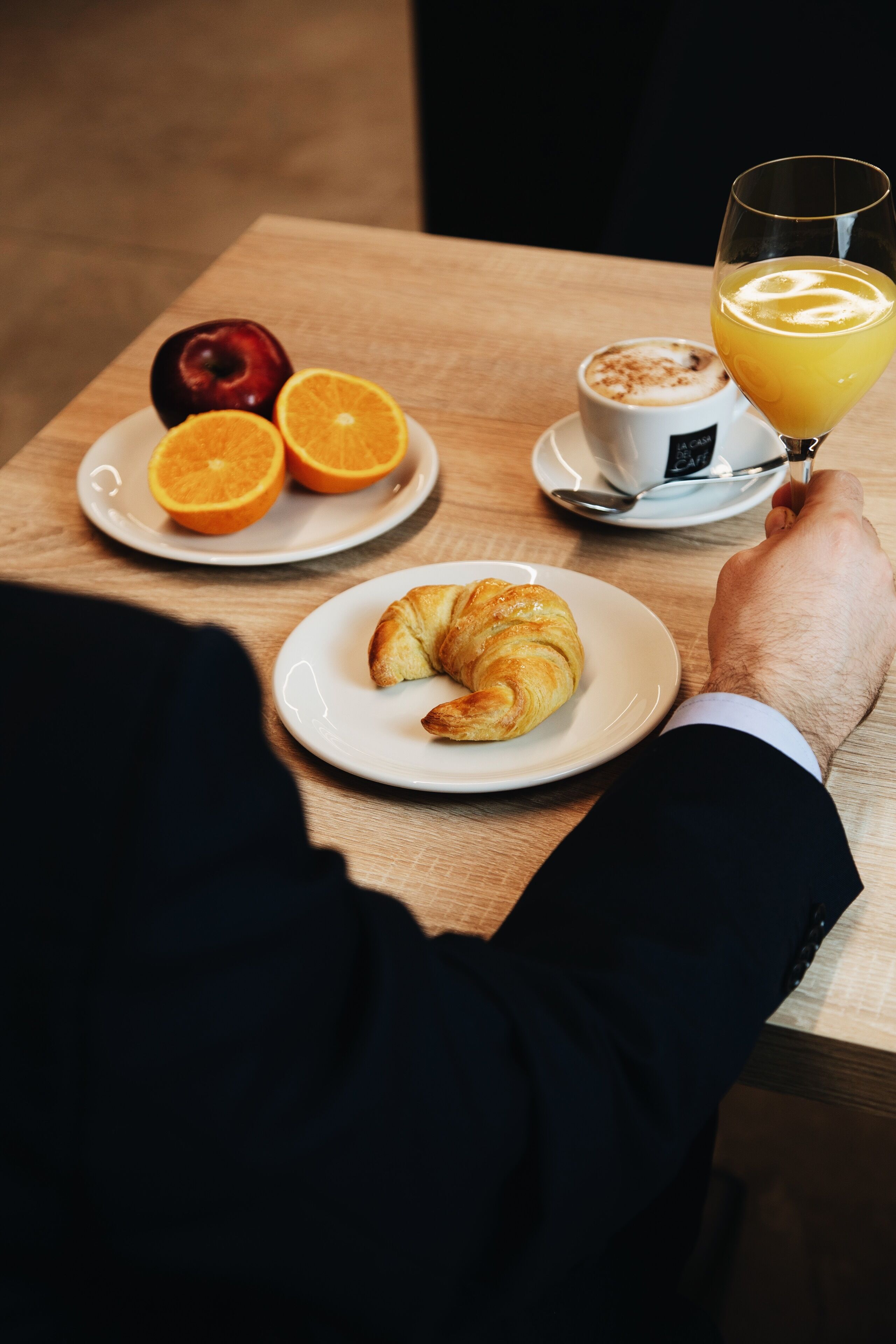 A table with a croissant, orange slices, and a cup of coffee.