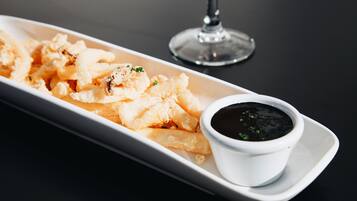 A white rectangular plate with fried calamari and a small bowl of black dipping sauce on a dark table.