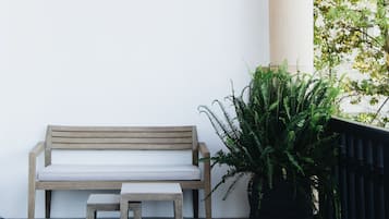 A bench and a small table in a covered outdoor area with a patterned floor, a large potted plant, and a column.